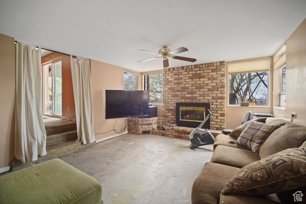 Living room featuring brick wall, concrete flooring, ceiling fan, and a fireplace