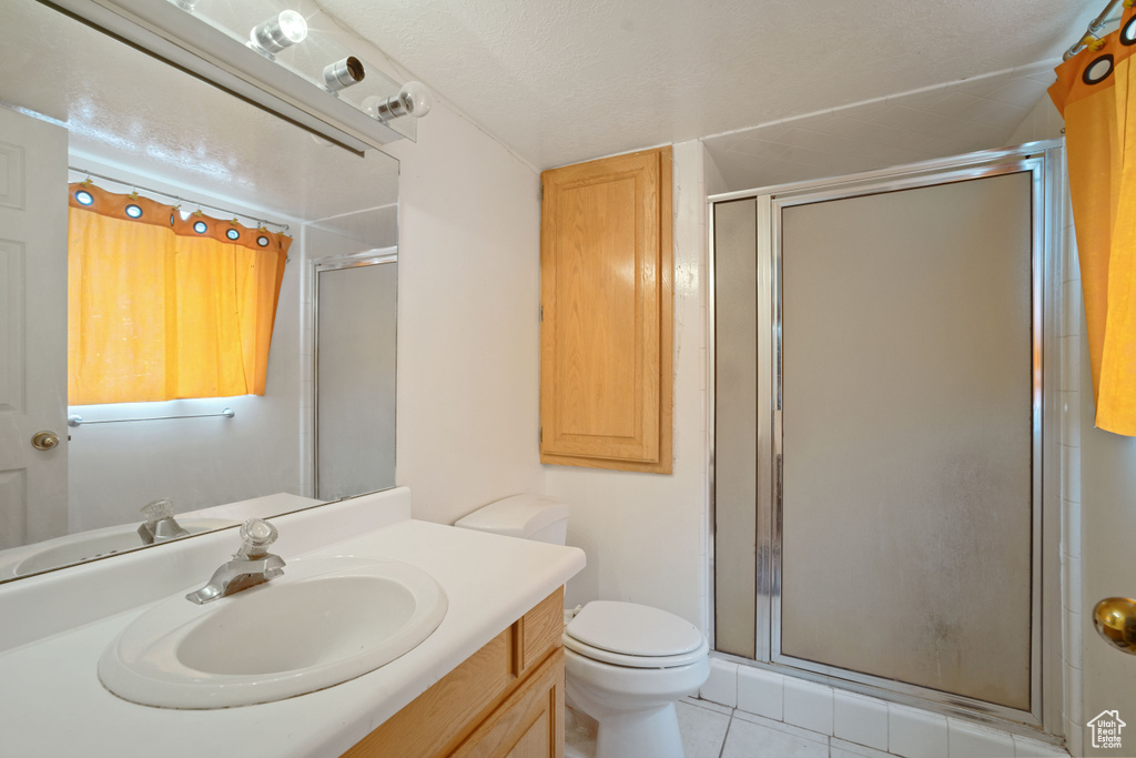 Bathroom featuring a shower with door, vanity, toilet, and tile floors