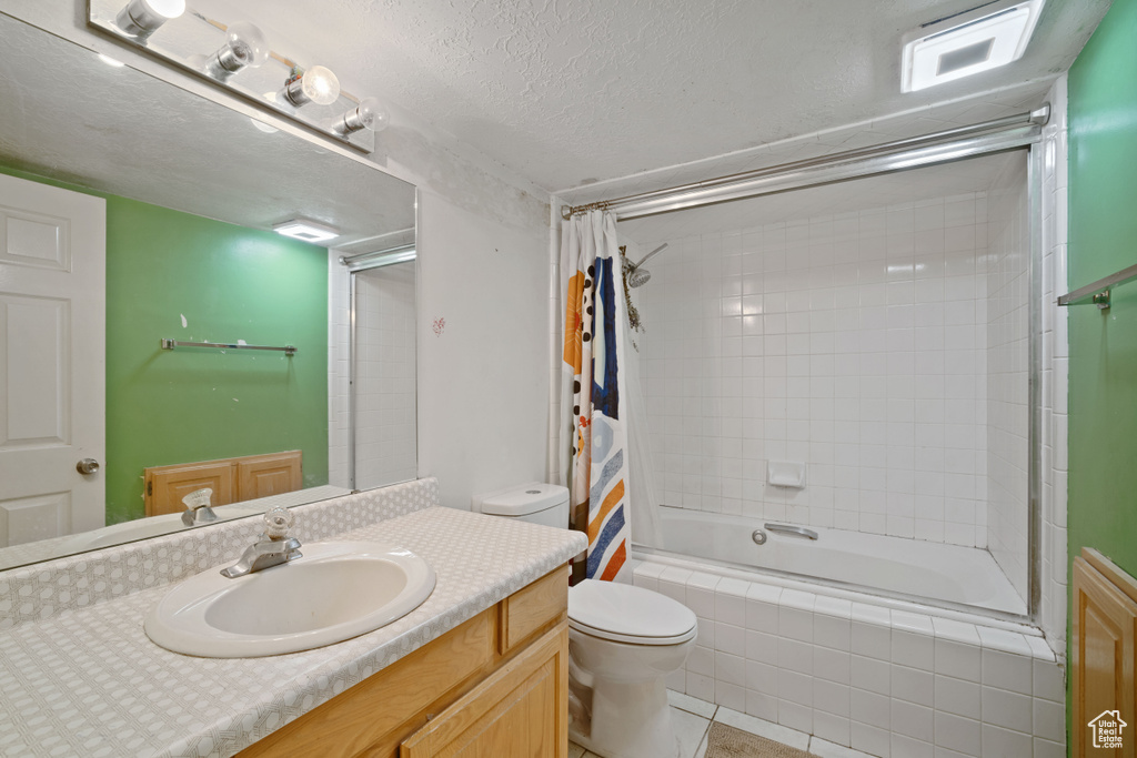 Full bathroom with vanity with extensive cabinet space, shower / bath combination with curtain, tile floors, toilet, and a textured ceiling