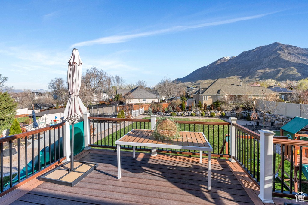 Wooden deck with a playground, a mountain view, and a yard