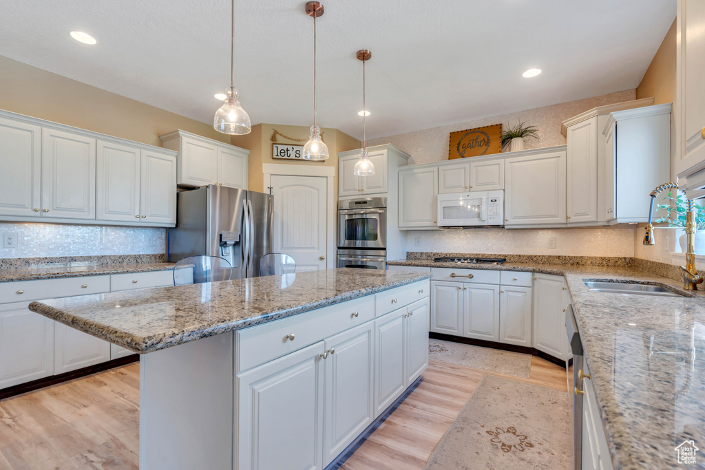 Kitchen with appliances with stainless steel finishes, light hardwood / wood-style flooring, white cabinetry, pendant lighting, and a center island