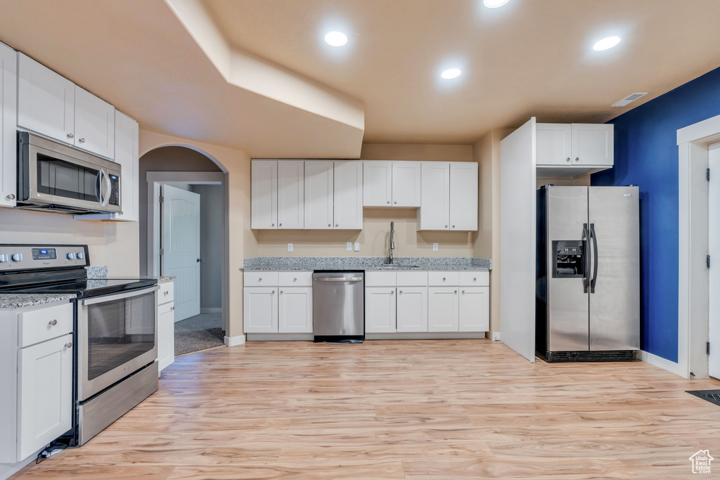Kitchen with appliances with stainless steel finishes, light hardwood / wood-style floors, white cabinetry, and light stone counters