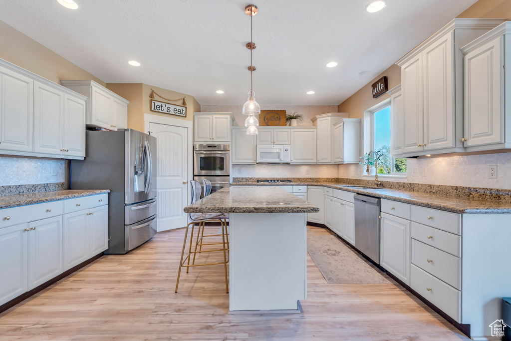 Kitchen featuring white cabinets, appliances with stainless steel finishes, a center island, and light hardwood / wood-style flooring