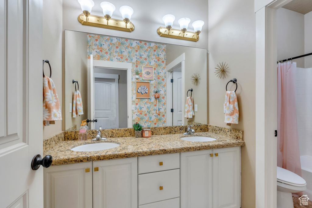 Full bathroom with oversized vanity, toilet, double sink, and shower / tub combo with curtain