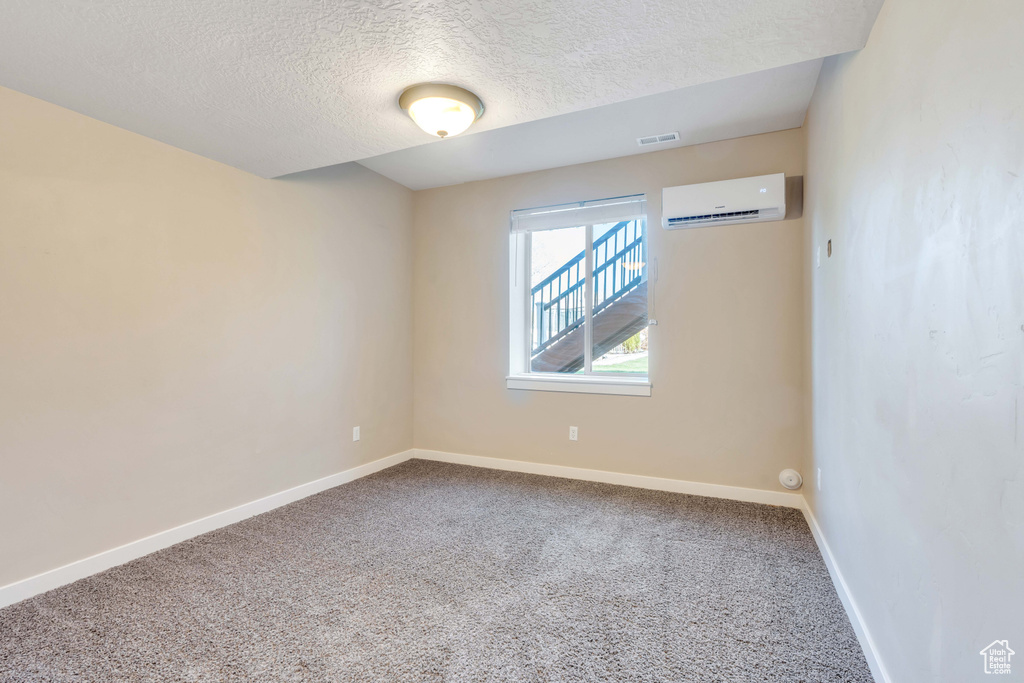 Empty room with a textured ceiling, a wall mounted AC, and carpet flooring