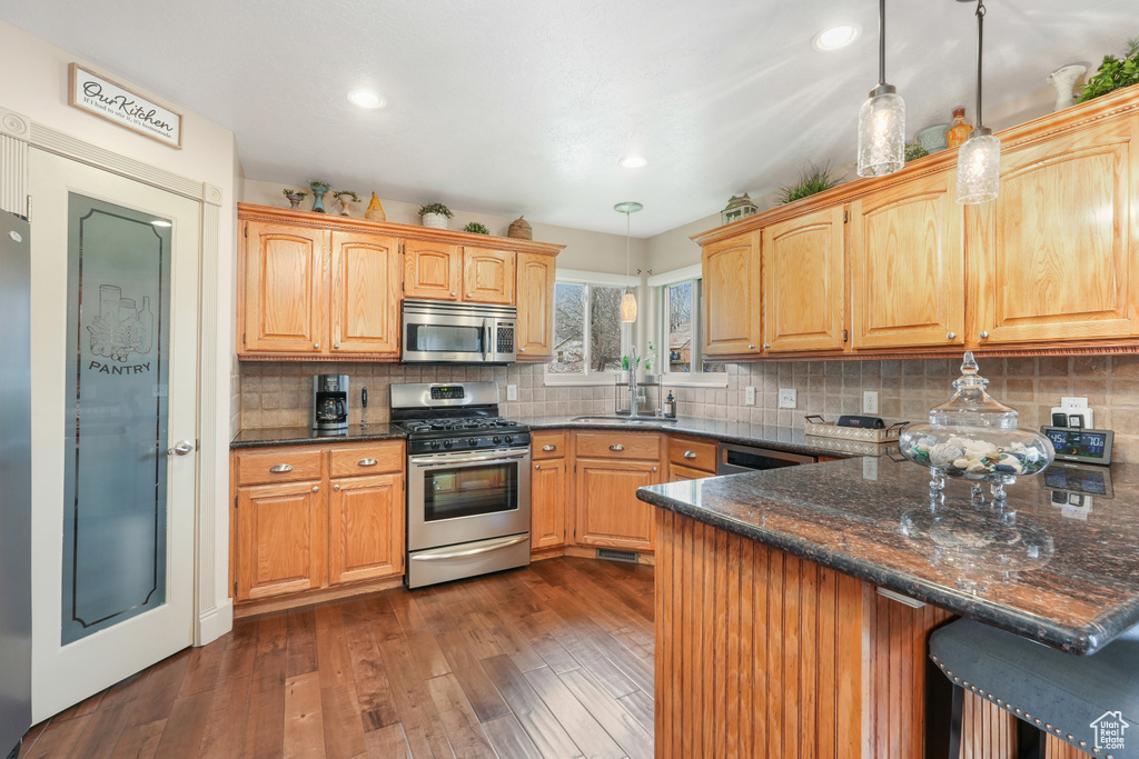 Kitchen with appliances with stainless steel finishes, backsplash, pendant lighting, and dark wood-type flooring