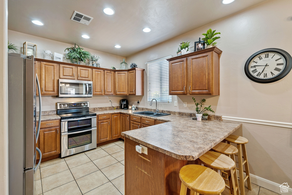Kitchen with a breakfast bar, light tile flooring, kitchen peninsula, stainless steel appliances, and sink