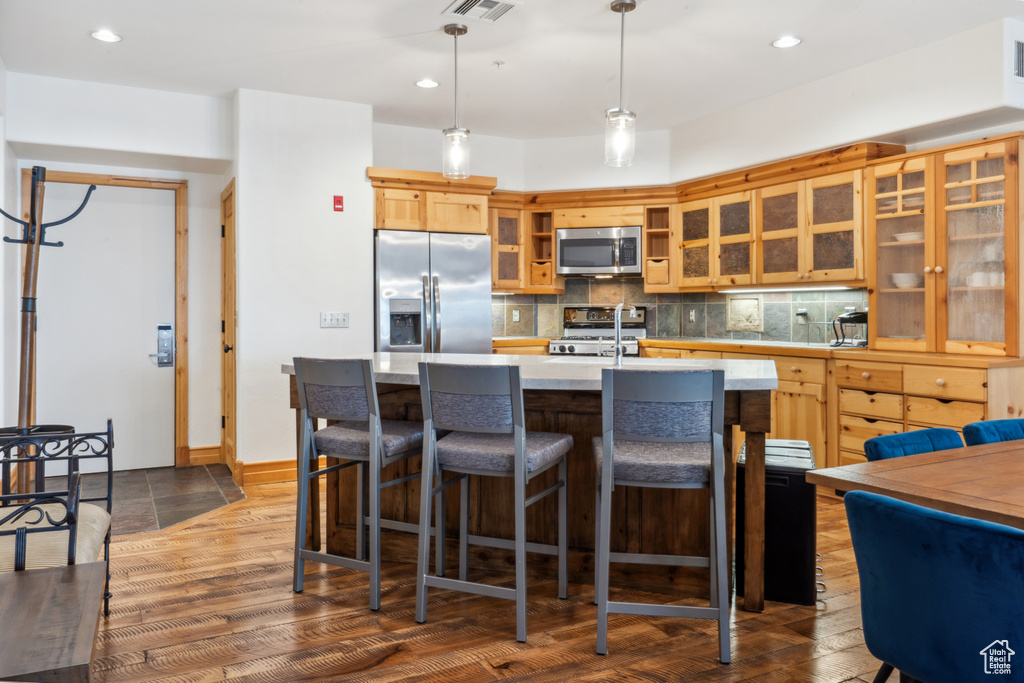Kitchen with a kitchen bar, appliances with stainless steel finishes, tasteful backsplash, an island with sink, and dark hardwood / wood-style flooring