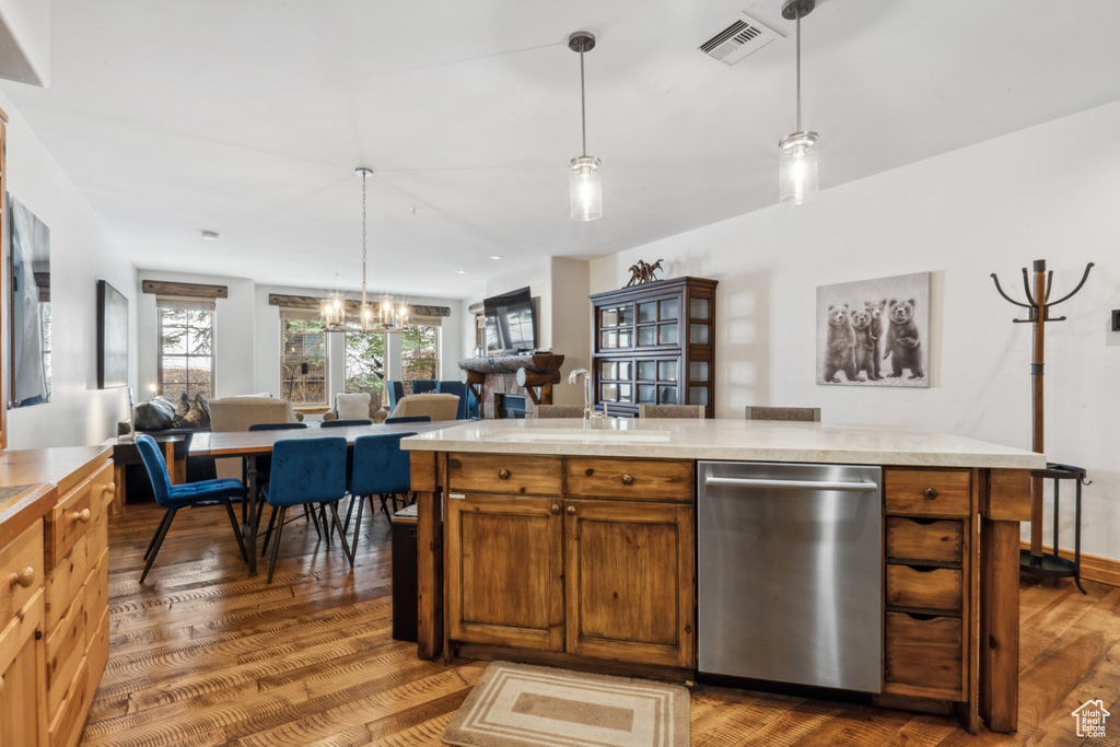 Kitchen featuring hanging light fixtures, wood-type flooring, sink, an inviting chandelier, and stainless steel dishwasher