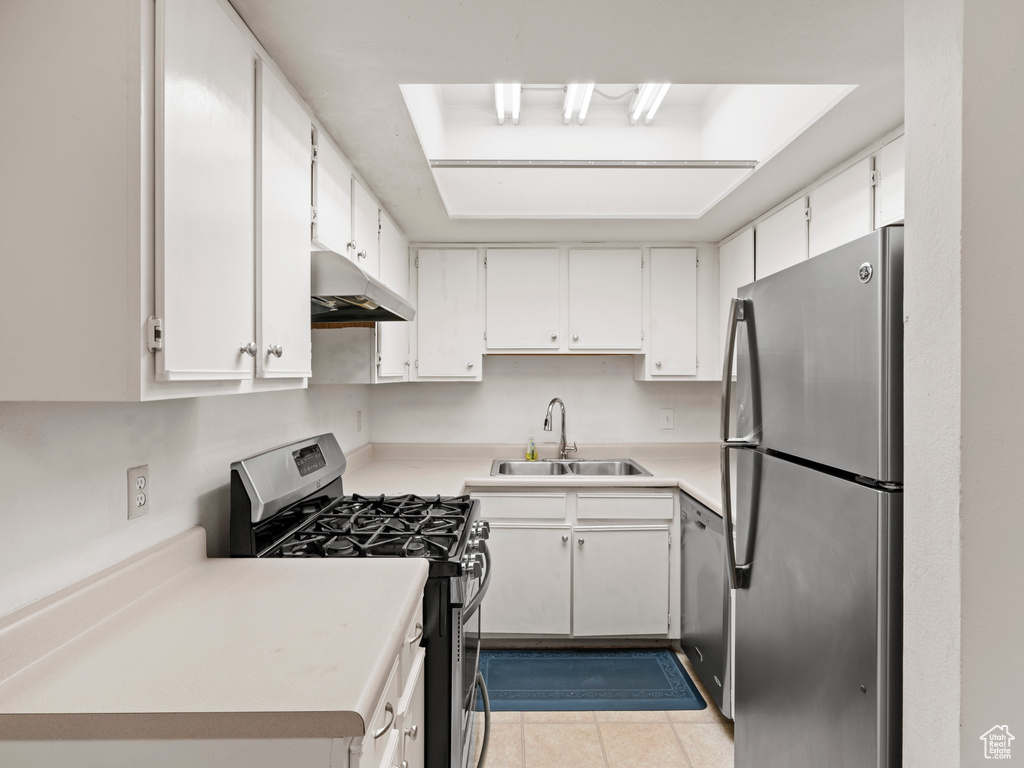 Kitchen with appliances with stainless steel finishes, sink, light tile floors, and white cabinets