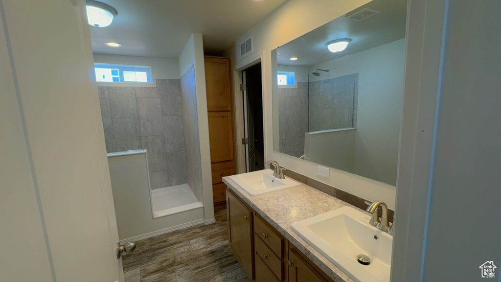 Bathroom with hardwood / wood-style flooring, tiled shower, and double sink vanity