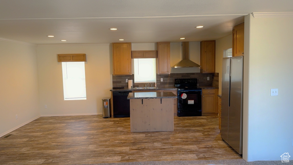 Kitchen featuring hardwood / wood-style flooring, wall chimney range hood, a center island, and black appliances