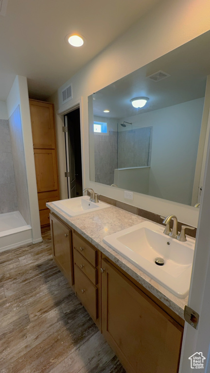 Bathroom featuring hardwood / wood-style floors, oversized vanity, tiled shower, and double sink