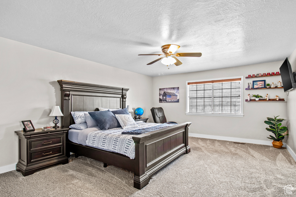 Bedroom with light colored carpet, ceiling fan, and a textured ceiling