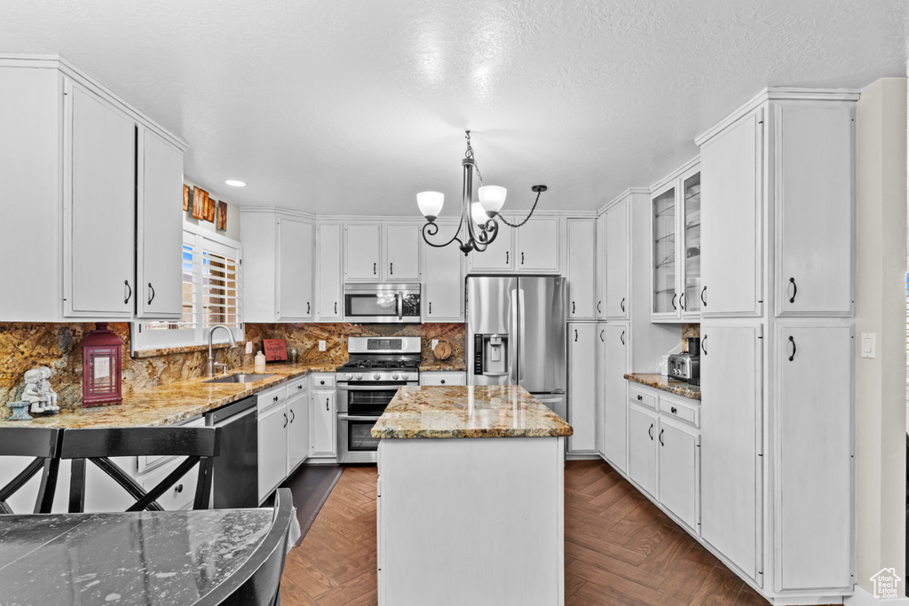 Kitchen with light stone counters, appliances with stainless steel finishes, a kitchen island, white cabinets, and dark parquet flooring