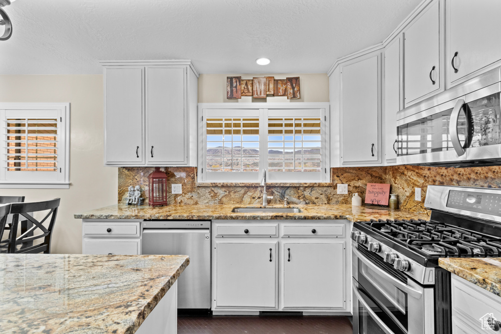 Kitchen with stainless steel appliances, sink, and light stone counters