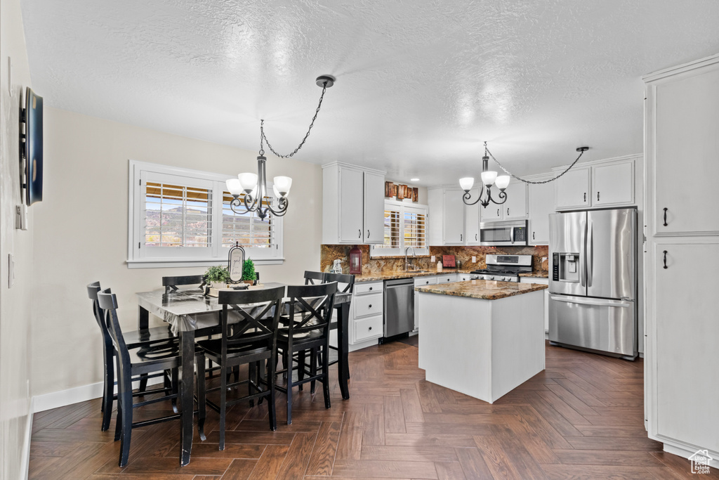 Kitchen featuring pendant lighting, white cabinetry, dark parquet flooring, appliances with stainless steel finishes, and a kitchen island
