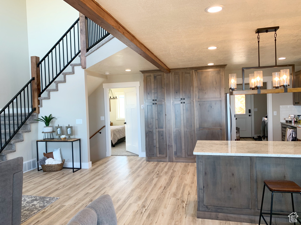 Kitchen with light hardwood / wood-style flooring, hanging light fixtures, a kitchen bar, and light stone countertops