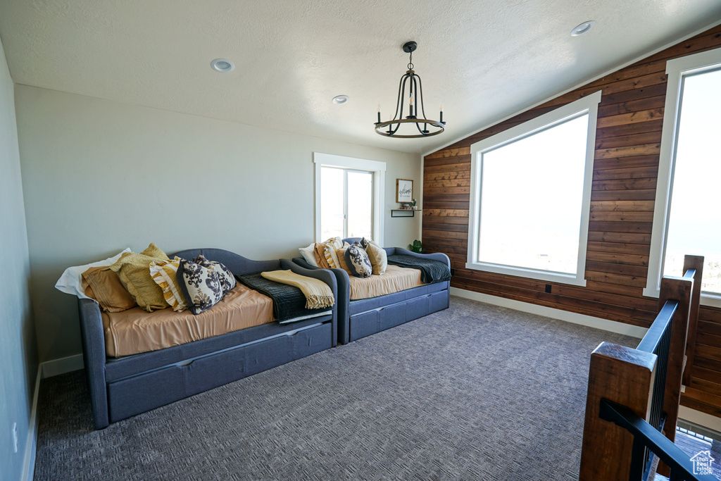 Living room featuring dark colored carpet, lofted ceiling, a textured ceiling, wooden walls, and a chandelier