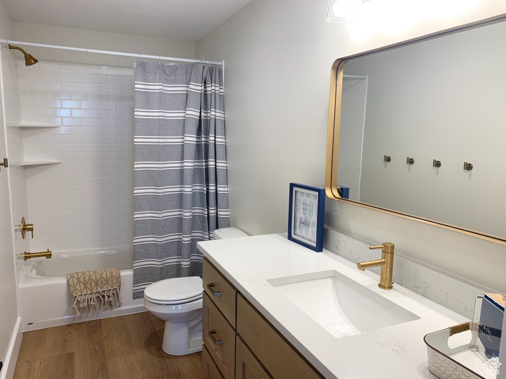 Full bathroom with wood-type flooring, large vanity, shower / tub combo, and toilet