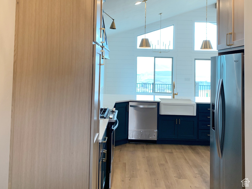 Kitchen with pendant lighting, light hardwood / wood-style flooring, appliances with stainless steel finishes, sink, and vaulted ceiling