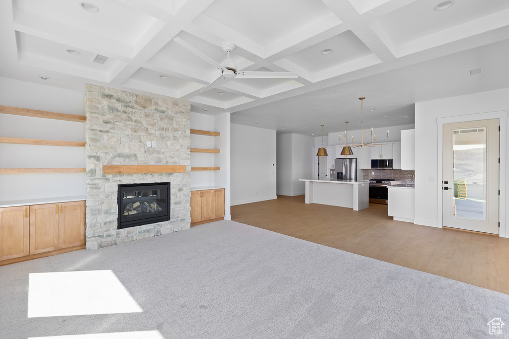 Unfurnished living room featuring coffered ceiling, a stone fireplace, ceiling fan, and light wood-type flooring