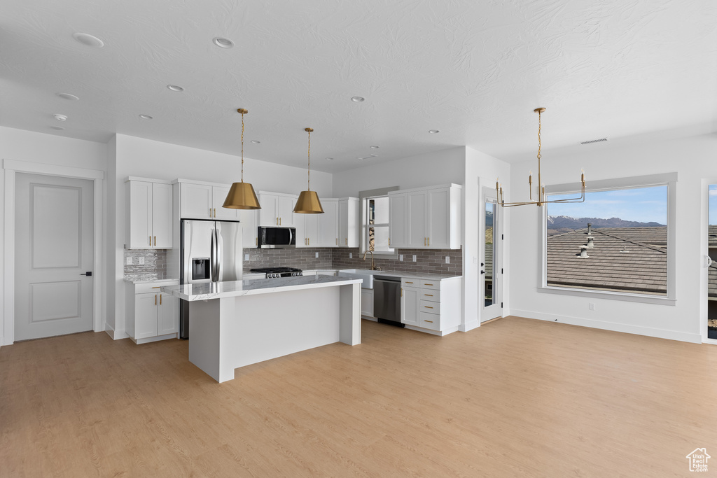 Kitchen featuring appliances with stainless steel finishes, a center island, a breakfast bar, white cabinets, and pendant lighting