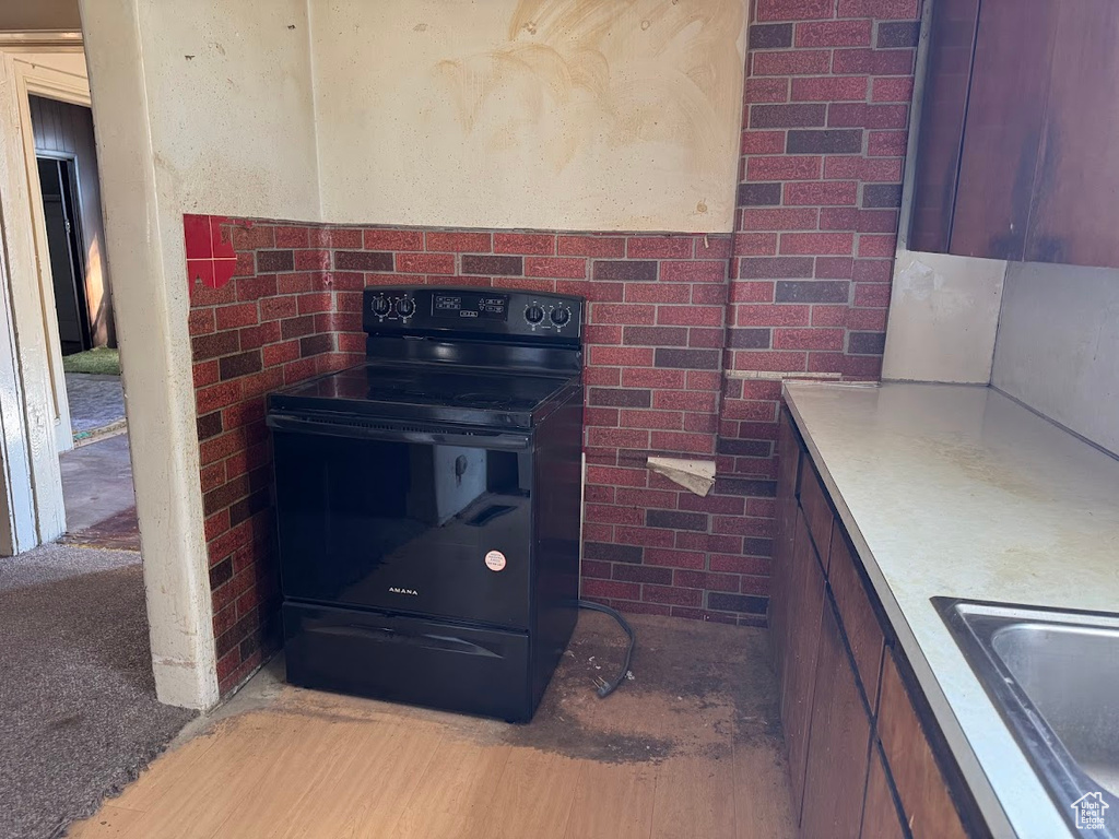 Kitchen with brick wall, black electric range, light hardwood / wood-style floors, and sink