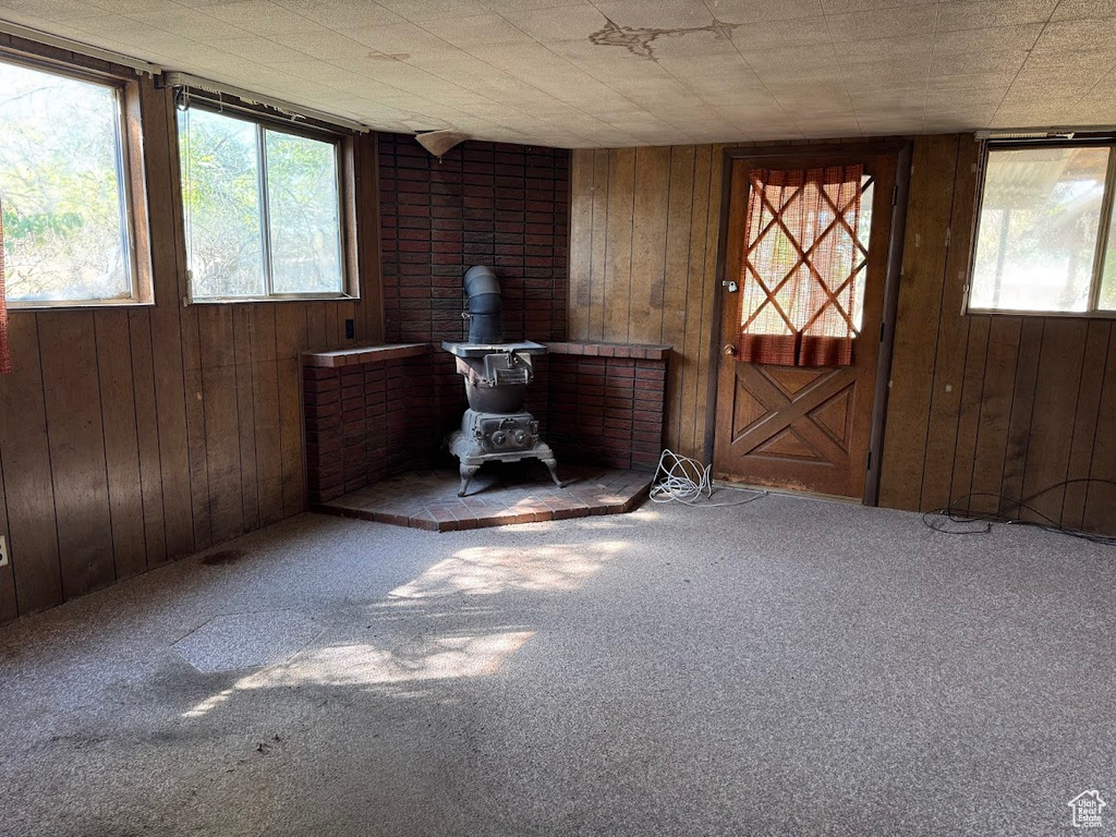 Carpeted empty room featuring a wood stove and wooden walls