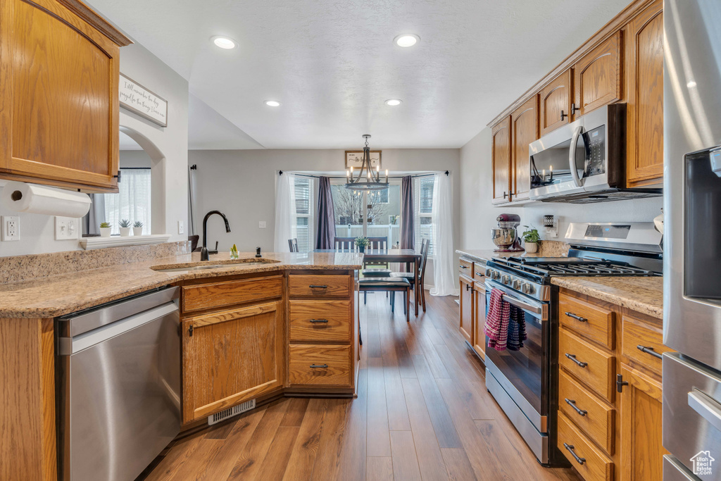 Kitchen with decorative light fixtures, light stone countertops, appliances with stainless steel finishes, sink, and light hardwood / wood-style floors