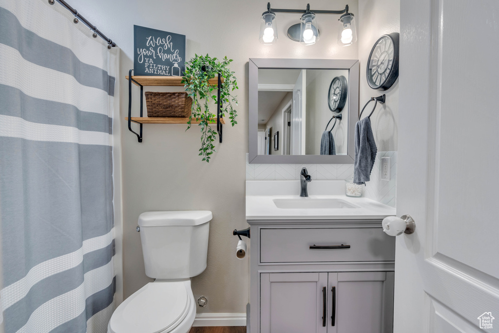Bathroom featuring backsplash, vanity with extensive cabinet space, and toilet
