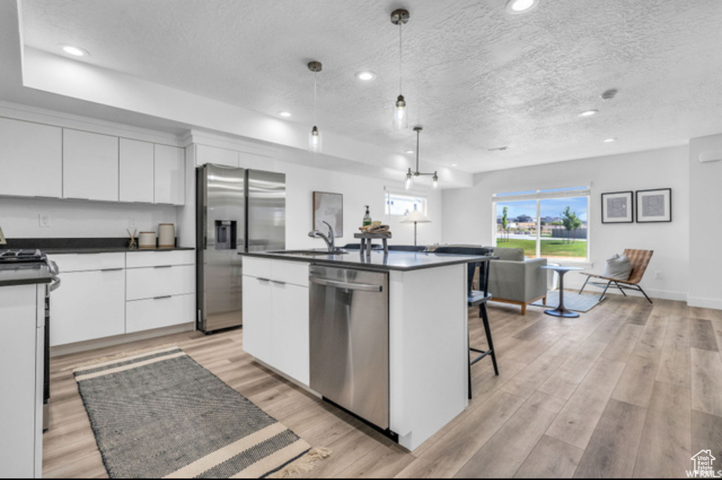 Kitchen featuring light wood-type flooring, stainless steel appliances, white cabinets, and hanging light fixtures