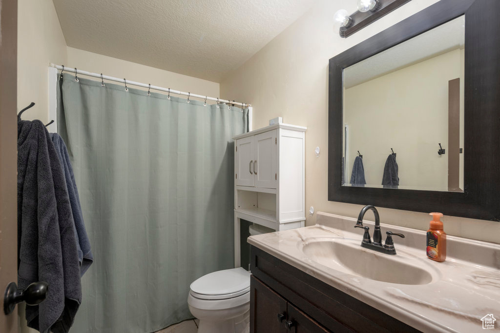 Bathroom featuring vanity with extensive cabinet space, toilet, and a textured ceiling