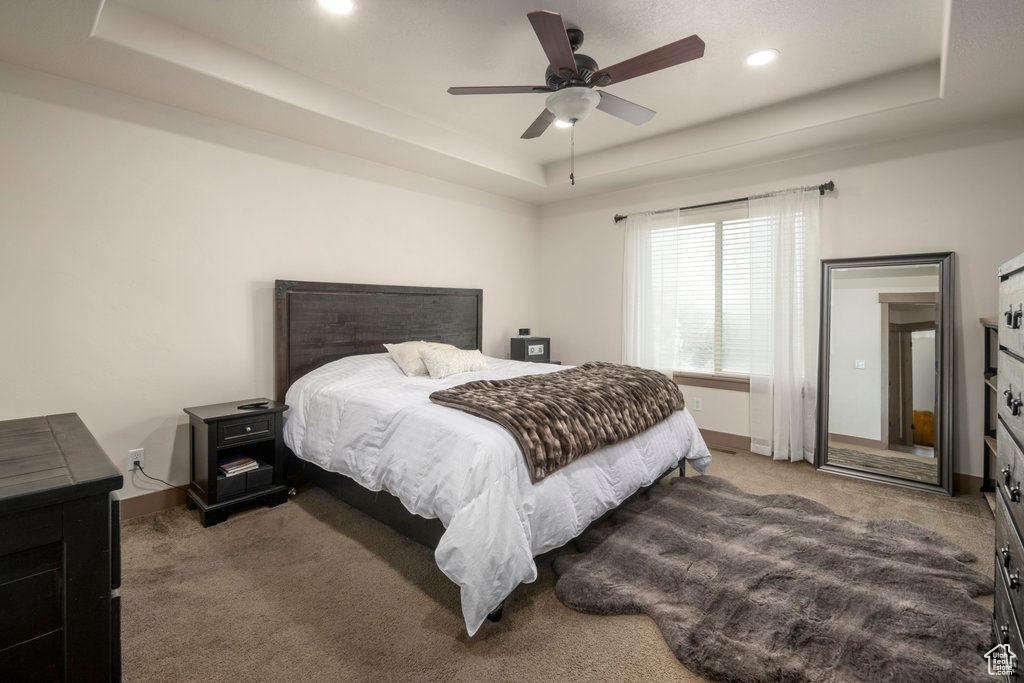 Bedroom with dark colored carpet, ceiling fan, and a tray ceiling
