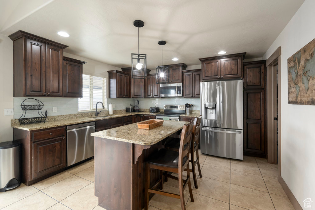 Kitchen with decorative light fixtures, appliances with stainless steel finishes, a kitchen island, light stone counters, and sink