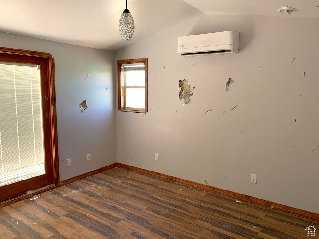 Empty room featuring vaulted ceiling, an AC wall unit, and hardwood / wood-style flooring