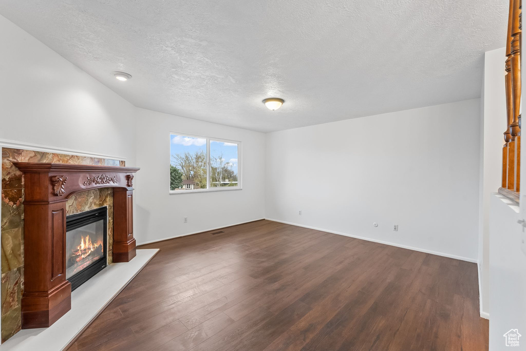 Unfurnished living room featuring a textured ceiling, dark hardwood / wood-style flooring, and a premium fireplace