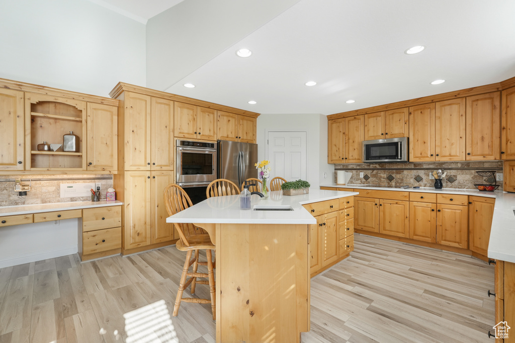 Kitchen featuring light hardwood / wood-style flooring, stainless steel appliances, tasteful backsplash, a kitchen island with sink, and sink