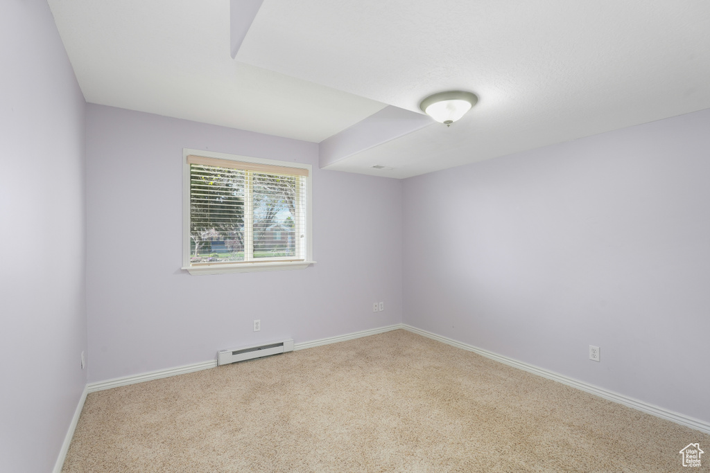 Carpeted spare room featuring a baseboard heating unit