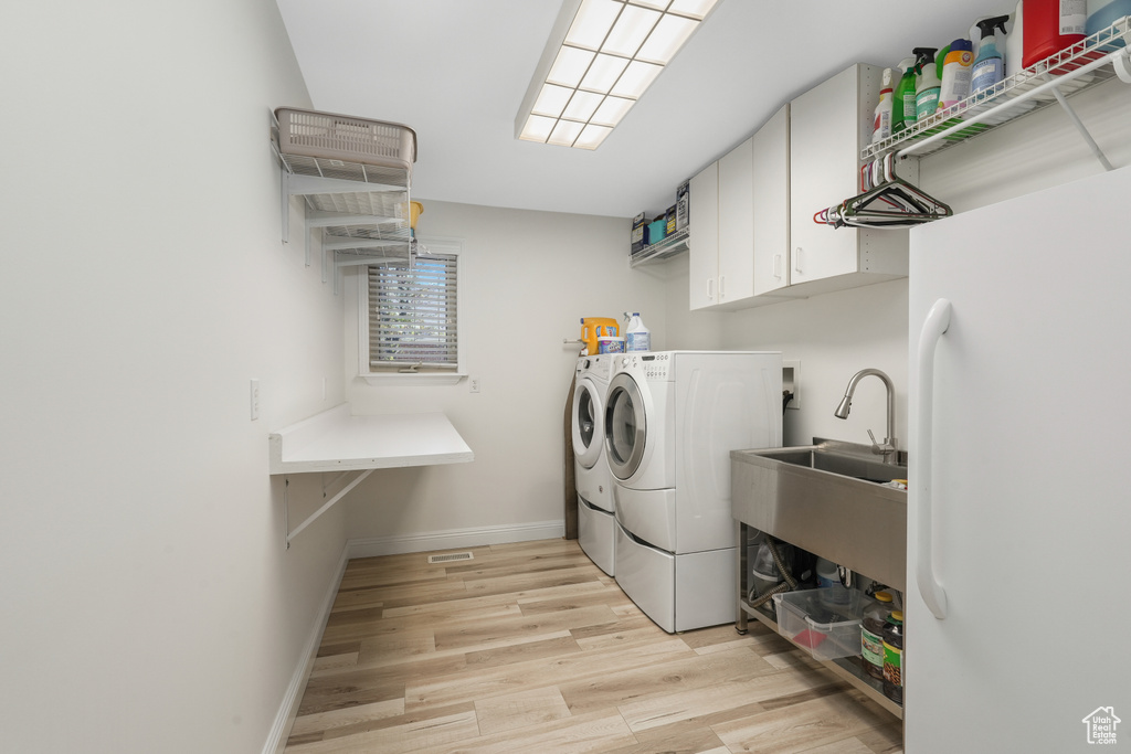 Washroom with light hardwood / wood-style flooring, washing machine and clothes dryer, cabinets, and sink