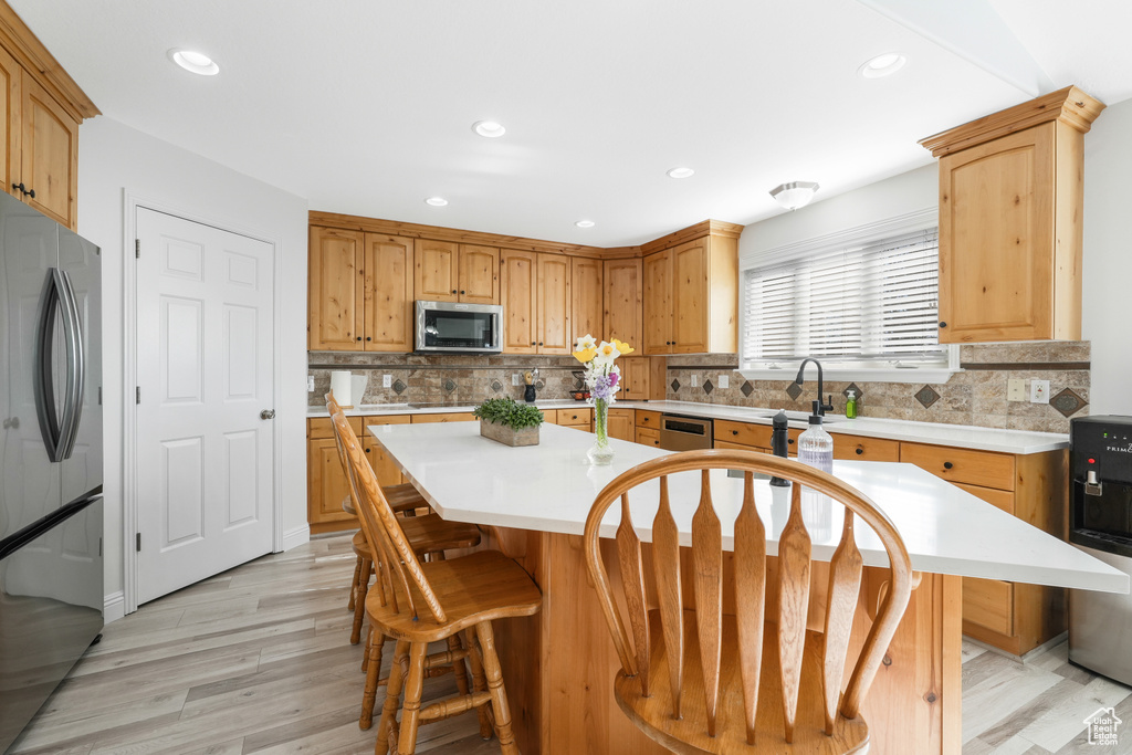 Kitchen featuring a center island, tasteful backsplash, appliances with stainless steel finishes, and light hardwood / wood-style floors