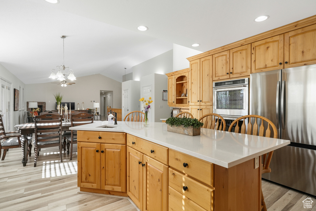 Kitchen with hanging light fixtures, an inviting chandelier, appliances with stainless steel finishes, vaulted ceiling, and light hardwood / wood-style floors