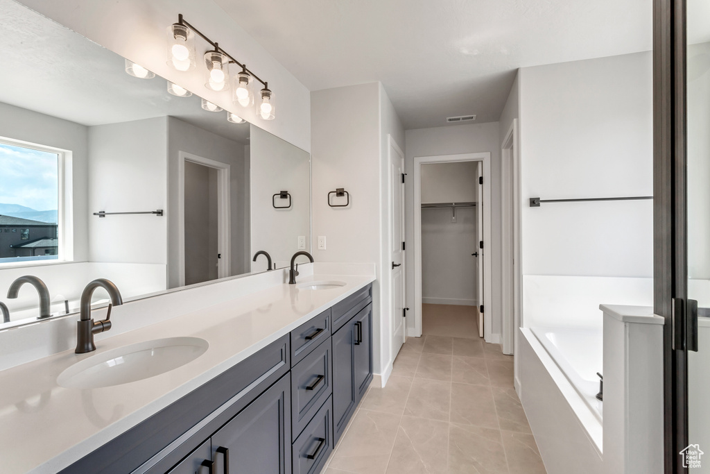 Bathroom featuring tile flooring, a tub, vanity with extensive cabinet space, and dual sinks