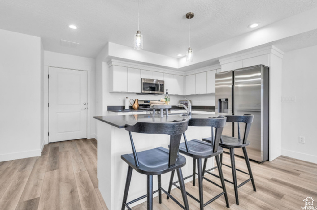 Kitchen with hanging light fixtures, light hardwood / wood-style flooring, stainless steel appliances, white cabinets, and a kitchen breakfast bar