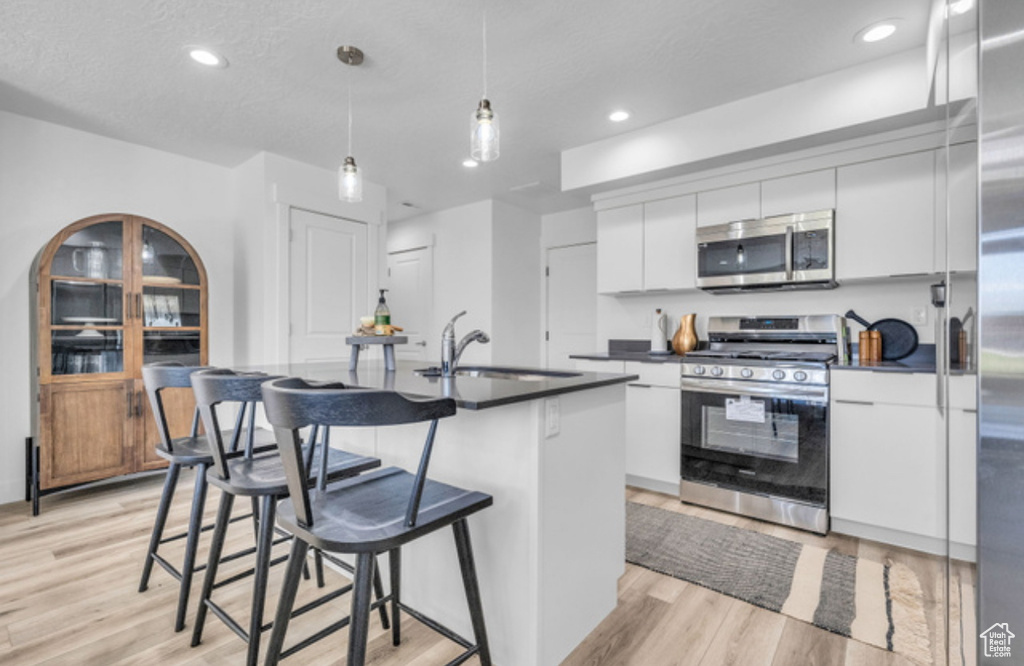 Kitchen featuring decorative light fixtures, light wood-type flooring, white cabinetry, appliances with stainless steel finishes, and a breakfast bar area