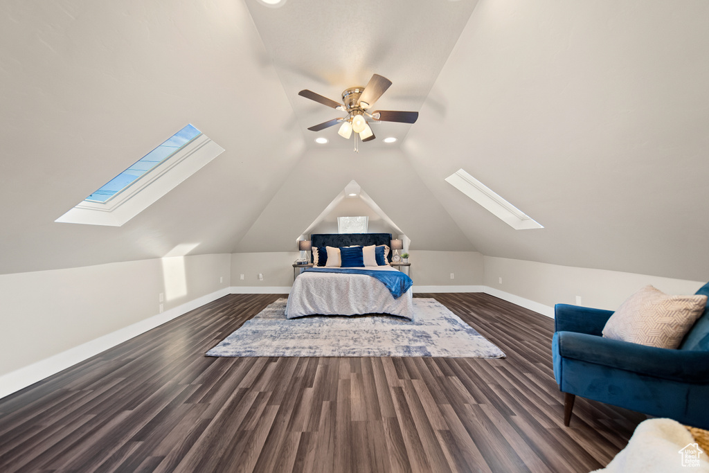 Unfurnished bedroom with ceiling fan, vaulted ceiling with skylight, and dark wood-type flooring