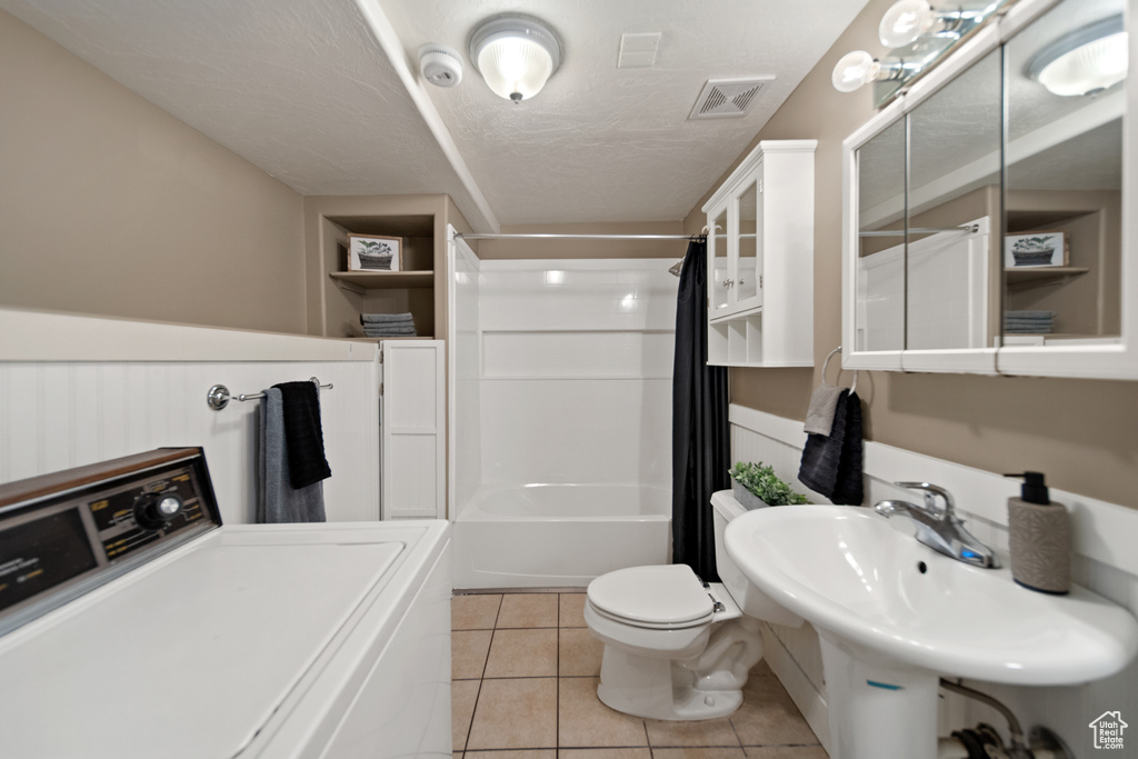 Interior space with sink, washer / dryer, shower / bath combo, toilet, and tile floors