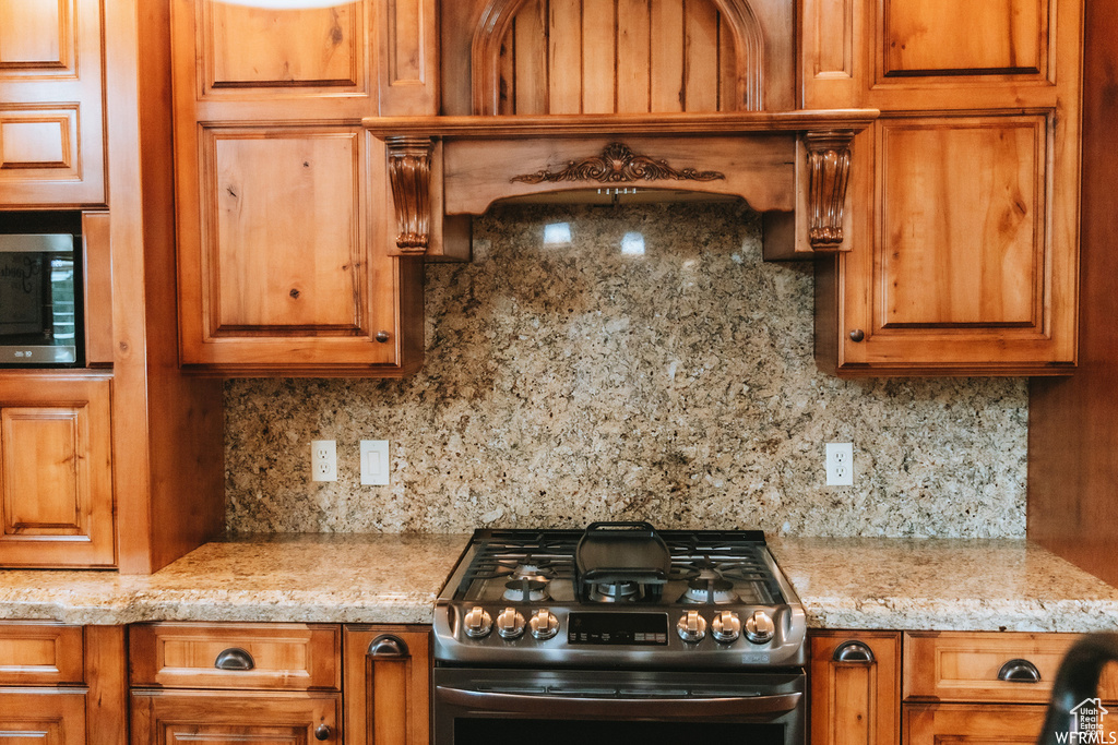 Kitchen featuring light stone counters, backsplash, and stainless steel range with gas cooktop