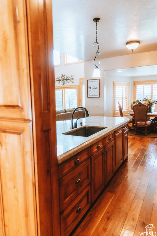 Kitchen featuring hardwood / wood-style flooring, hanging light fixtures, sink, and light stone counters