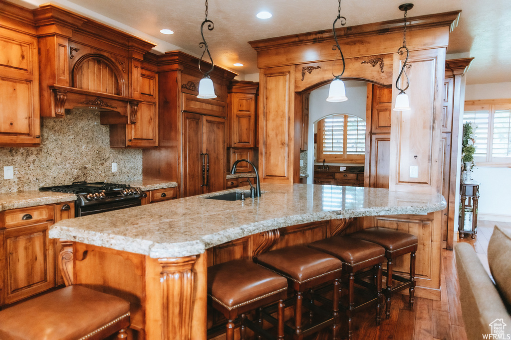 Kitchen featuring pendant lighting, black gas range oven, dark wood-type flooring, sink, and a breakfast bar area